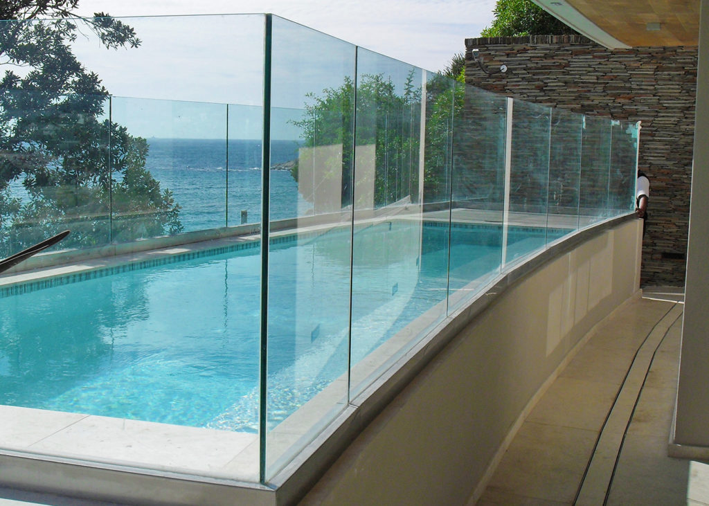 Curved frameless glass pool safety barrier beside a swimming pool with sea views