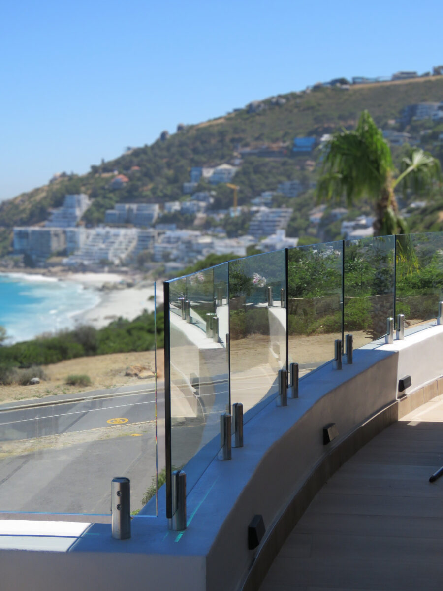Frameless glass balustrade curving along a clifftop terrace overlooking a Cape Town beach