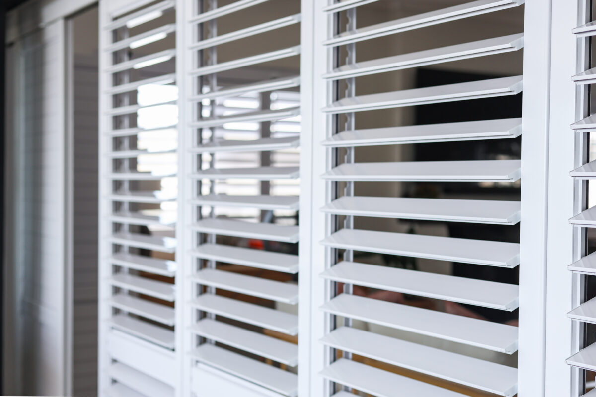 White aluminium security shutters with adjustable louvres fitted across a patio sliding door