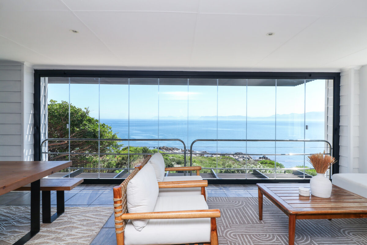 Frameless glass stacking doors along a covered balcony overlooking the ocean