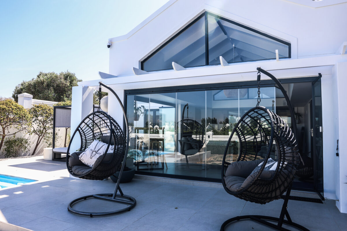 Frameless glass sliding doors opened onto a poolside patio at a white Cape Town home